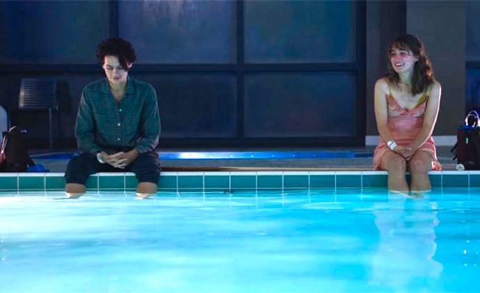 Casal adolescente sentado na beira de uma piscina.