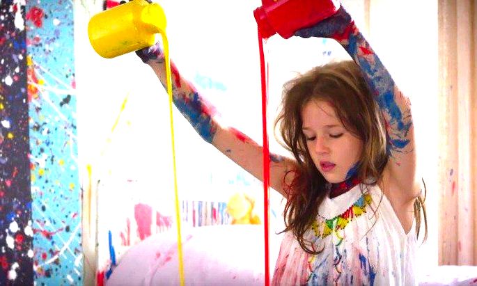 Criança, toda suja de tinta colorida, pintando.