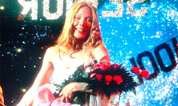 Carrie no baile da escola, recebendo flores e uma faixa de rainha do baie