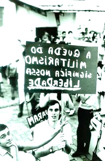 Foto de um protesto de 1968, jovem segura um cartaz pedindo o final do militarismo.
