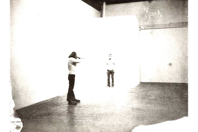 Homem apontando uma arma para outro homem. Performance Shoot, de Chris Burden