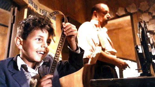 Cena de filme Cinema Paradiso exibe menino olhando negativos de cinema