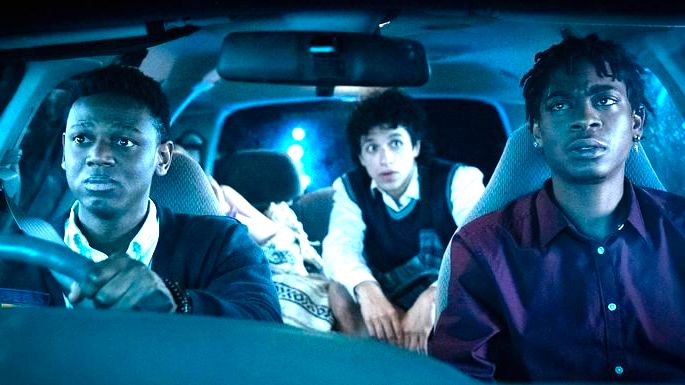 Três adolescentes dentro de um carro, com expressões preocupadas.