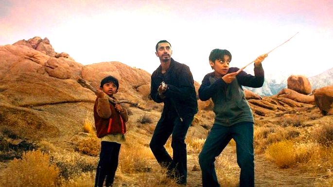Um homem e dois garotos num local deserto, se protegendo com paus nas mãos.