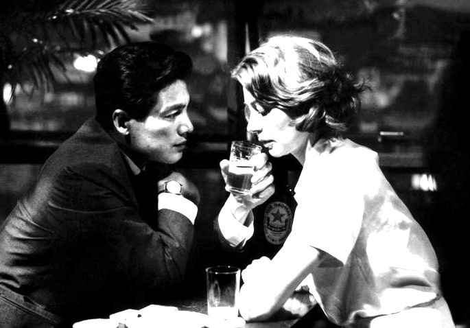 Fotografia em preto e branco de um casal num bar, bebendo cerveja, frente a frente