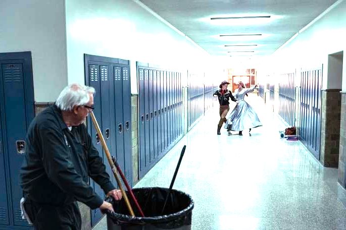 Zelador vendo casal dançando no corredor da escola