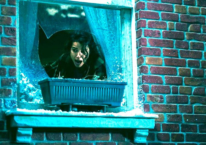 Mulher gritando na janela de uma casa com o vidro quebrado.