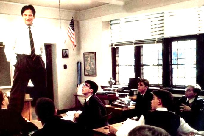 Professor dando aula de pé, em cima da mesa.