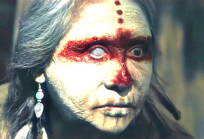 Mulher mais velha, indígena, com o rosto pintado e uma expressão assustadora